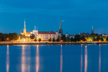 Fototapeta na wymiar Riga, Latvia. Panoramic Picturesque Urban View Of Daugava Or Western Dvina River In Central Part Of City With Famous Landmarks In Bright Illumination Under Blue Sky In Summer Night