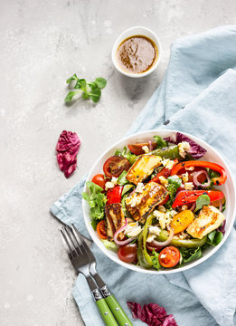 Vegetable salad cherry tomatoes, baked pepper, salad mix and onion with grilled haloumi (halloumi) cheese. Keto diet, healthy food. Light grey stone background. Top view.