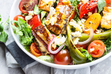 Vegetable salad cherry tomatoes, baked pepper, salad mix and onion with grilled haloumi (halloumi) cheese. Keto diet, healthy food. Light grey stone background. Close up.