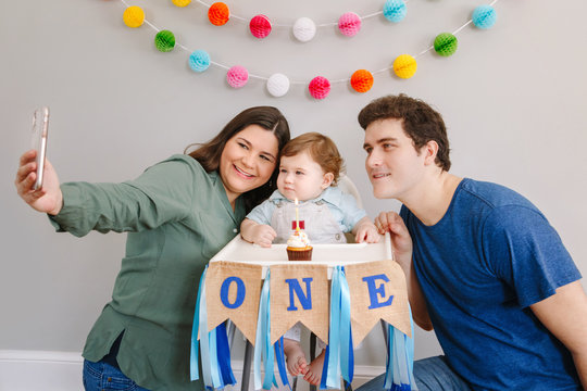 Mother father dad taking selfie with child kid toddler. Caucasian family with baby boy celebrating first birthday at home. Cupcake dessert with one candle. Happy birthday lifestyle concept.