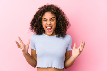 Young african american woman against a pink background screaming with rage.