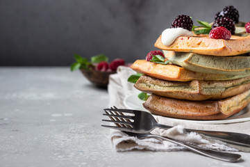 A stack of homemade Belgian waffles with frozen berries, mint and natural greek yogurt on a white plate, light grey stone background. 