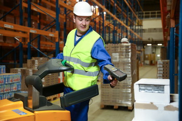 warehouse worker on a forklift scans a box of goods with a barcode scanner