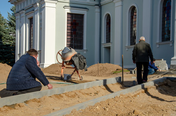 Grodno, Belarus, October 21, 2018: a group of builders engaged in the repair of a Catholic church. Laying a new sidewalk. Chief engineer points to problems in the work.