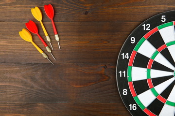 darts and dartboard on wooden background flat lay
