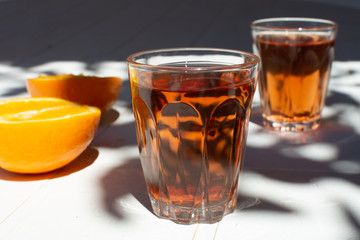 Greek wine in 2 glasses, fresh ripe orange served in garden in sun lights