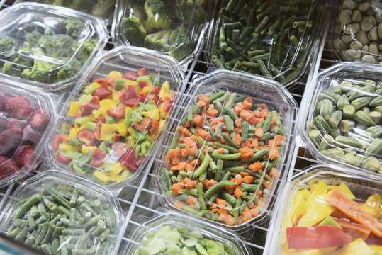 Frozen vegetables, fruits and berries. Food products are poured into rectangular plastic trays.