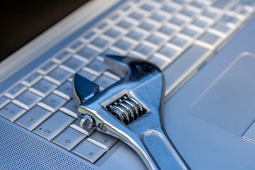 Adjustable wrench next to a silver laptop. Computer service, maintenance theme.