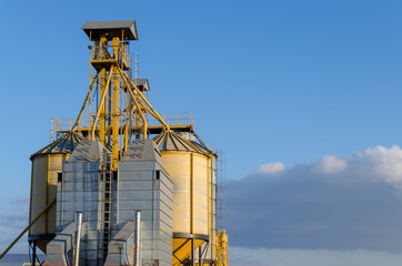 Fototapeta na wymiar A large modern plant for the storage and processing of grain crops. view of the granary on a sunny day. Large iron barrels of grain against the sky. End of harvest season.