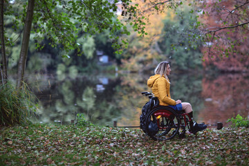 A disabled woman sits thoughtfully in a wheelchair by the lake.