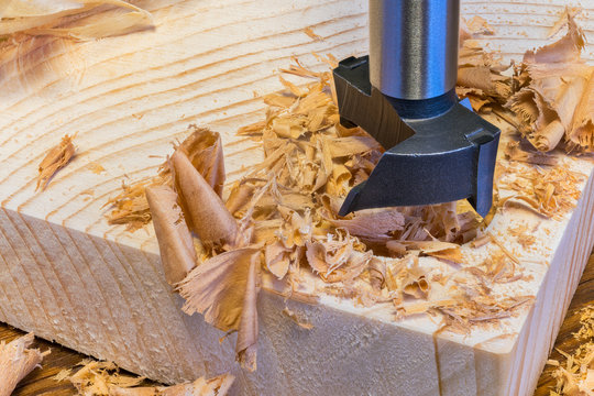 Steel Forstner drill bit. Boring of cylindrical hole into wooden plank. Sharp cutting tool detail. Drilling in wood by precise milling cutter. Beautiful pile of scattered curled shavings. Woodworking.