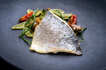Gebratenes italienisches Fisch Filet von der Dorade mit Spinat Pasta, Queller und Tomaten als closeup auf einem Modern Design Teller