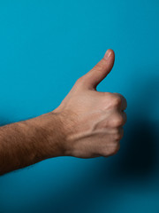 Closeup of male hand showing thumbs up sign against blue background