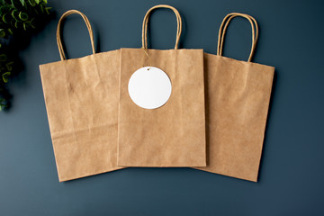 Three paper kraft bags with a blank gift tag on a blue background mockup