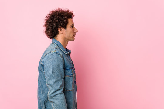 Curly mature man wearing a denim jacket against pink background gazing left, sideways pose.