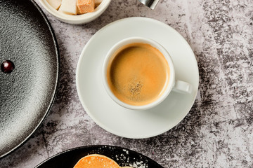 Cup of americano coffee with pancakes and sour cream cake for breakfast. A cup of black coffee in a white cup, shot from above, with copyspace. Food and drink concept.