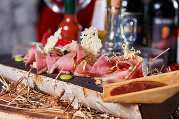 Antipasto on wooden plate close up. Cold smoked meat plate with tomato hot sauce, sliced ham, prosciutto, bacon. Appetizer on wooden tray cut tree sawed imitation.