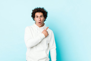 Young sporty man against a blue background pointing to the side