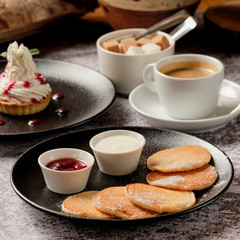 tasty pancakes with cupcakes with whipped cream and a cup of black coffee americano for breakfast. Small round fritter with sour cream, berry jam and black tea cup on the background. Food and drink