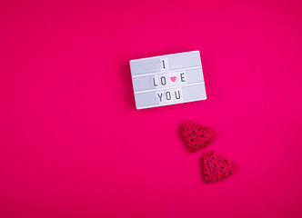 Words i love you on the light box on a pink background with hearts.