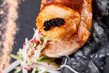 Scallops and ravioli. Seafood, pike perch fish, caviar and black dumplings in a plate on a dark table close-up. Healthy food.