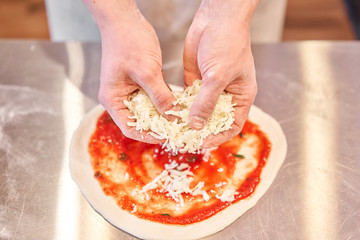 Cooking pizza. arranges cheese ingredients on the dough preform. Closeup hand of chef baker in uniform white apron cook at kitchen