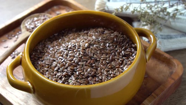 Flax seed poured in slow motion into rustic bowl. Flaxseed is an organic and healthy grain packed with natural nutrients often used in a vegetarian diet. 