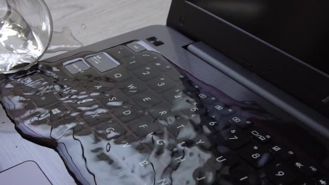 Water being spilled over laptop by accident. Keyboard is full of liquid and the computer is ruined. Slow motion shot.