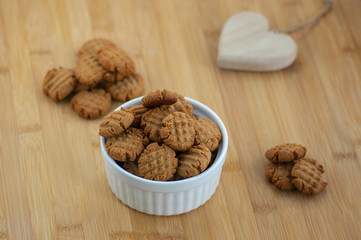 Very tasty peanut butter biscuits on bamboo wooden board in white baking bowl and decorative wood heart, golden baked healthy