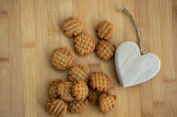Very tasty peanut butter biscuits on bamboo wooden board with decorative wood heart, golden baked healthy