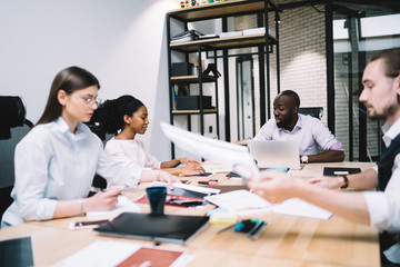 Coworkers sitting at desk doing paperwork and sharing ideas for project in afternoon