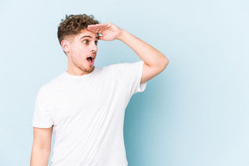 Young blond curly hair caucasian man isolated looking far away keeping hand on forehead.