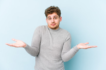 Young blond curly hair caucasian man isolated doubting and shrugging shoulders in questioning...