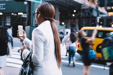 Focused black businesswoman walking on city street with smartphone