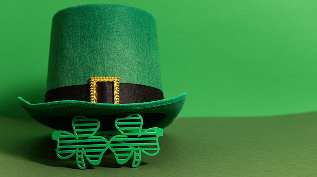Happy St Patricks Day. Lepricon hat with glasses in the shape of a three leaf clover on a green background. Holiday attributes