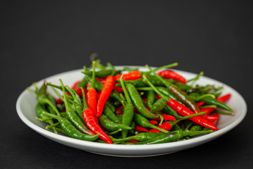Pile of green and red chili de arbol peppers on flat plate. Organic home grown vegetables ripening. Black background.