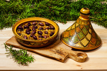 Moroccan tagine dish in open traditional tagine pot with black olives on the top. Tagine placed on...