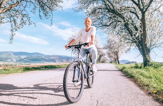 Happy smiling man riding a bicycle on the country road under blossom trees. Spring is comming concept image.