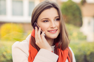 Cellphone talk. Beautiful woman talking on the phone outdoors and smiling toothy smile. mixes race asian russian model on green city scape background at the station in city of Brussels Belgium