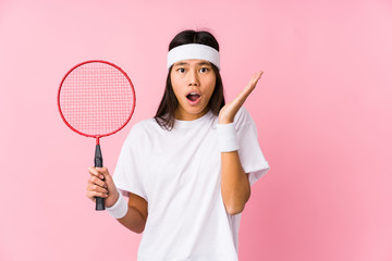 Young chinese woman playing badminton in a pink background surprised and shocked.
