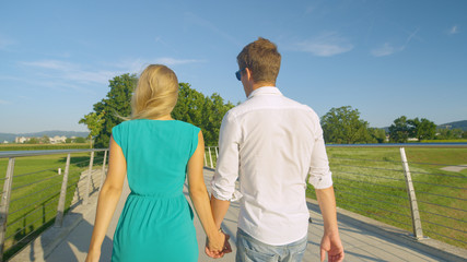 CLOSE UP: Unrecognizable couple holding hands walks across a bridge in a park.