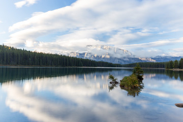Banff National Park Lake with single tree island and cloudy skies reflecting in the water