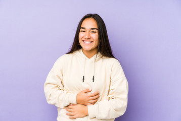 Young woman isolated on a purple background laughs happily and has fun keeping hands on stomach.