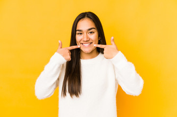 Young woman isolated on a yellow background smiles, pointing fingers at mouth.