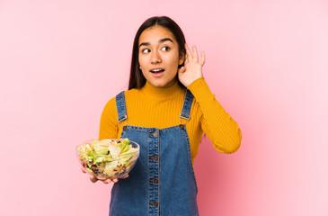 Young asian woman holding a salad isolated trying to listening a gossip.