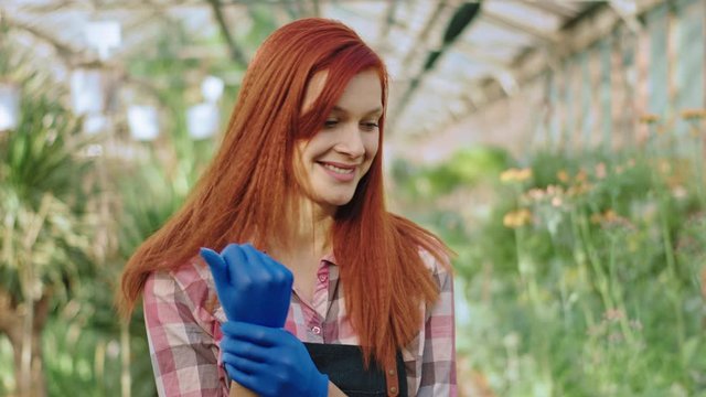 Redhead charismatic gardener lady wearing her blue gloves before start to take care after her decorative plants she looking straight to the camera and smiling large. Shot on ARRI Cinema Camera
