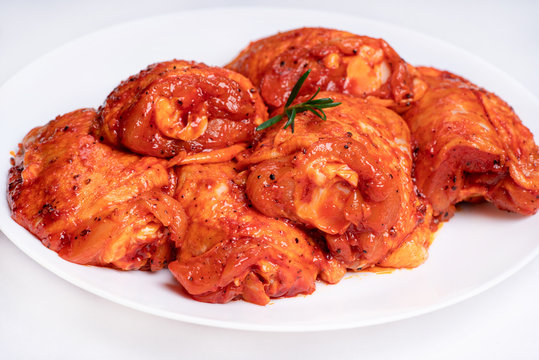 Chicken legs in a red marinade on a white plate. Top view. Chicken meat close-up.Dietary meat. Cooking.Raw marinated chicken legs for grill and bbq.Isolate.