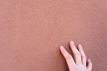 Empty background. Orange wall, porous texture. The fingers of the young guy touch the surface of the painted wall of the building. Fingers close up.