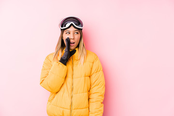 Young caucasian woman wearing a ski clothes in a pink background is saying a secret hot braking news and looking aside