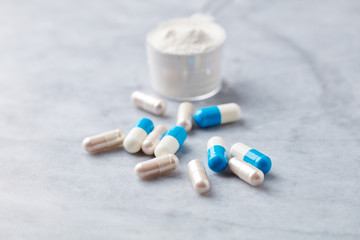 Sport supplements (carnitine and creatine capsules) and Scoop of whey protein on bright stone background. Close up. 